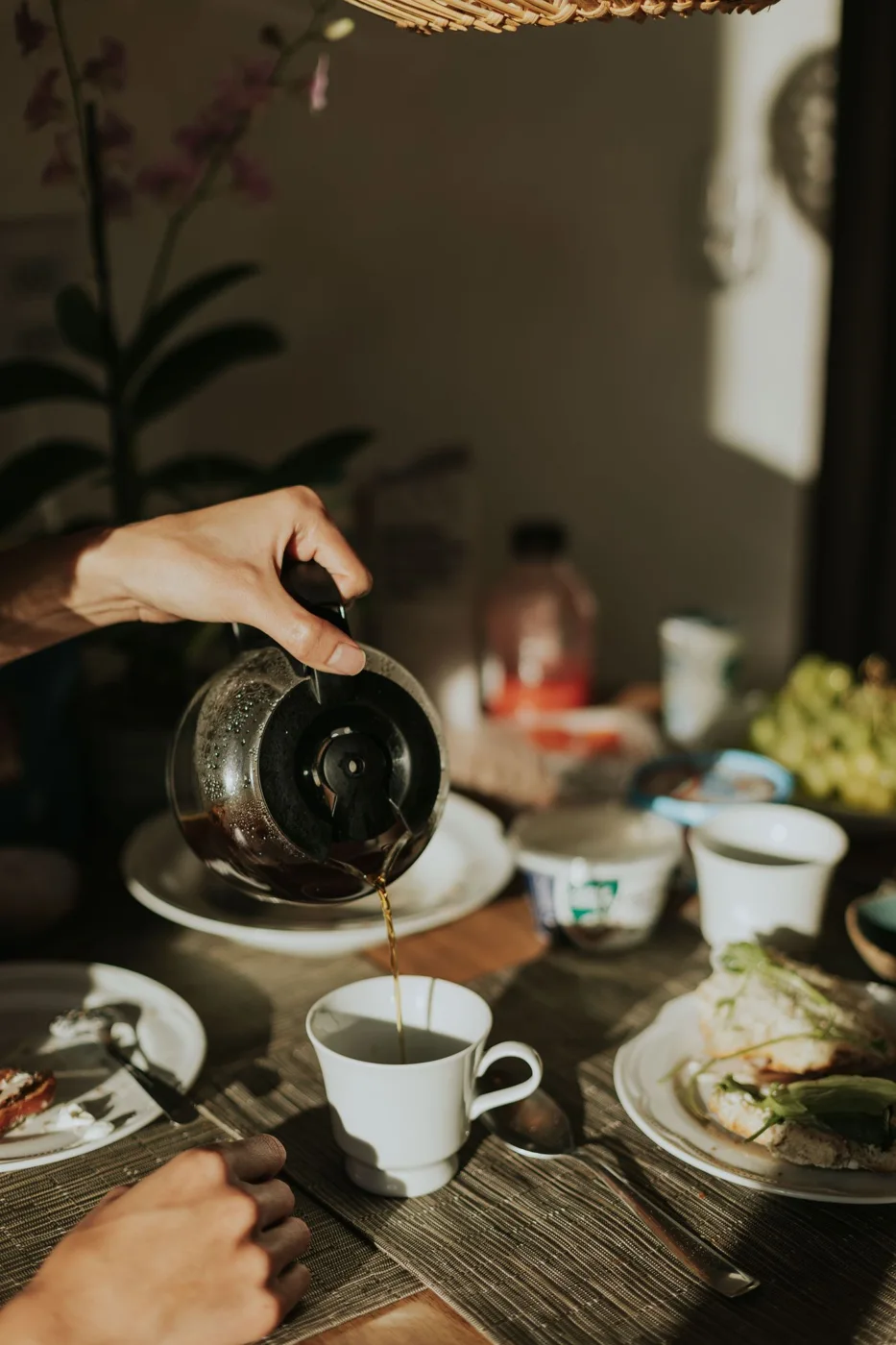 Coffee being poured beside cups and food at a breakfast table