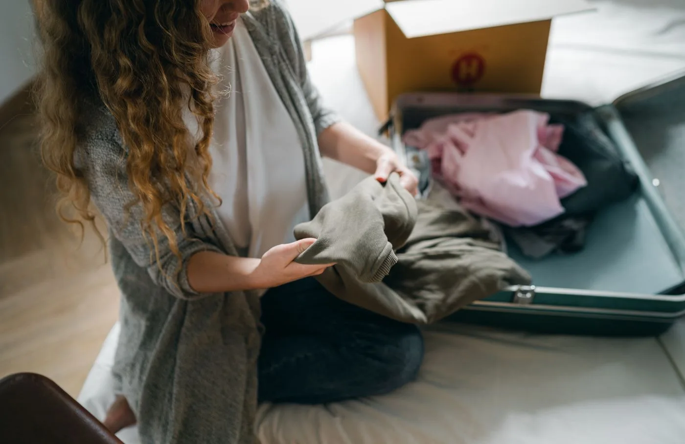 Woman arranging folded garments in an open suitcase on a bed