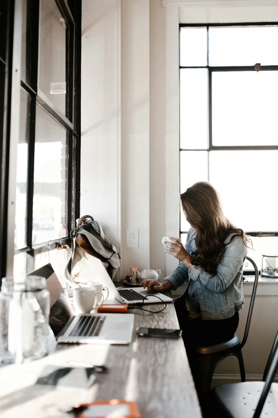 Woman using a laptop at a cafe counter beside tall windows