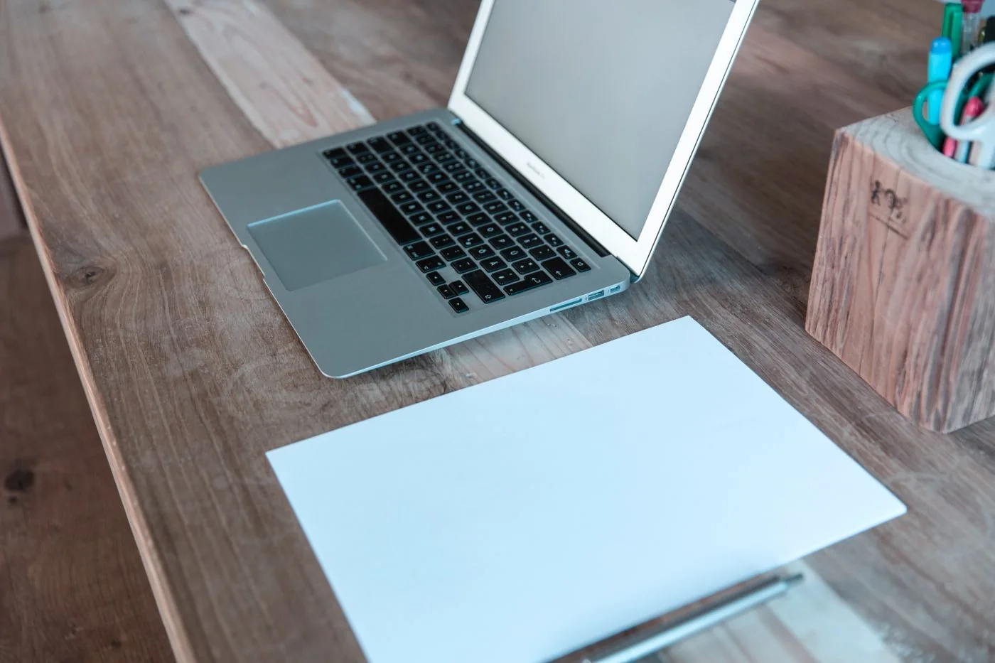 Open laptop beside a blank sheet of paper on a wooden desk