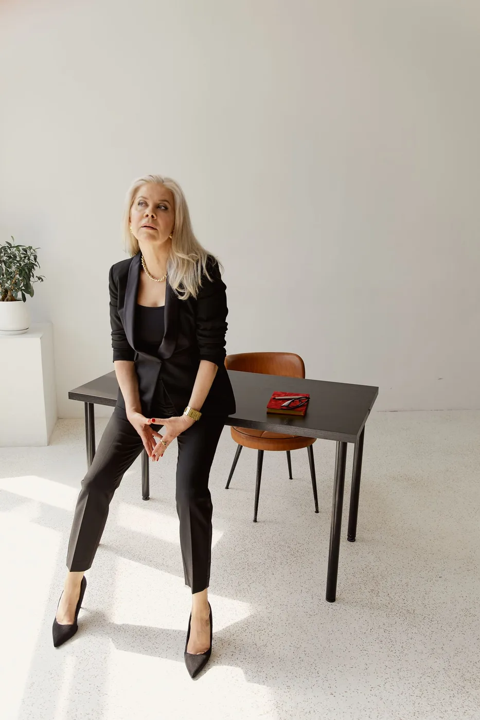 Woman in dark tailoring standing beside a wooden table