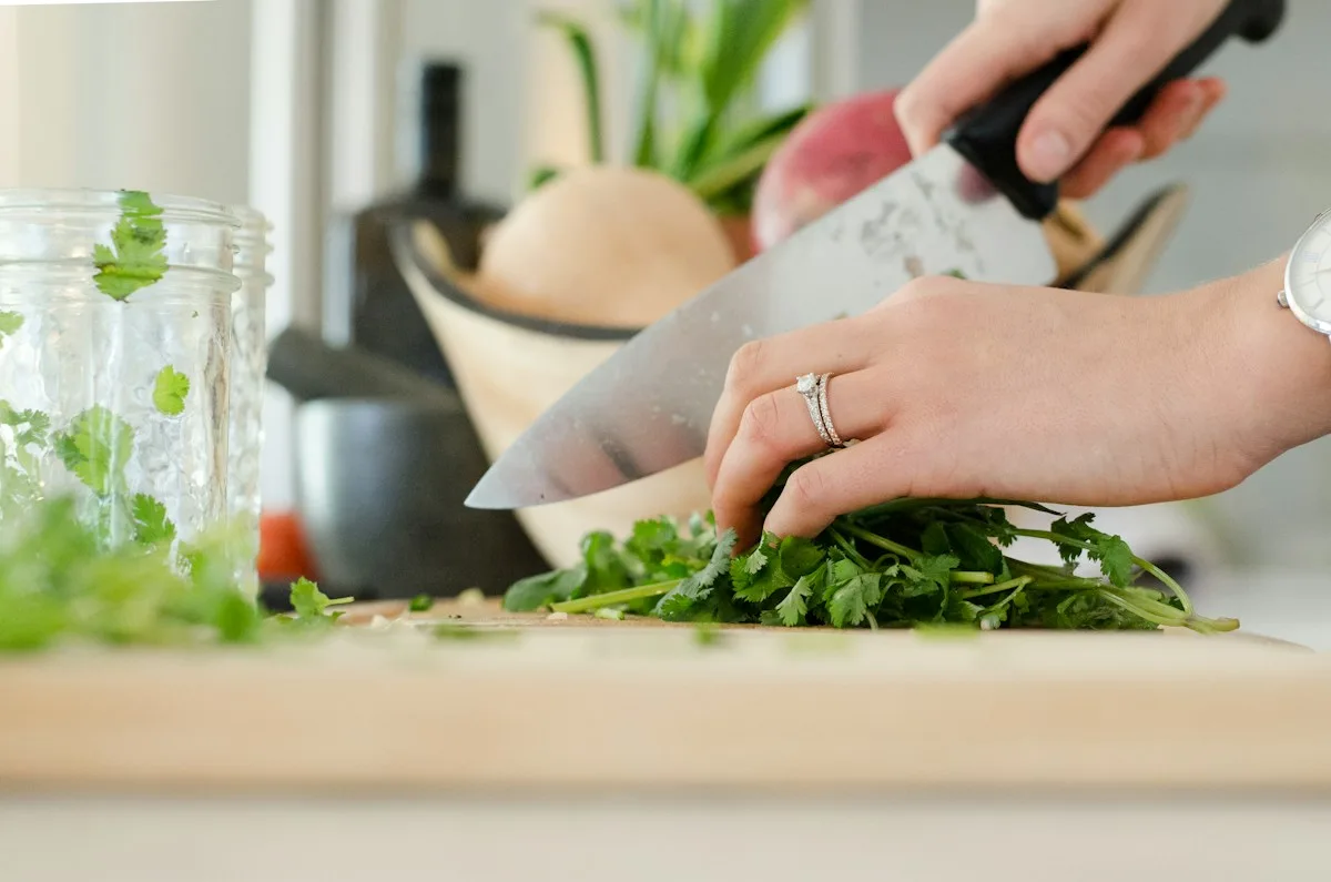 Hands chopping green herbs on a wooden board