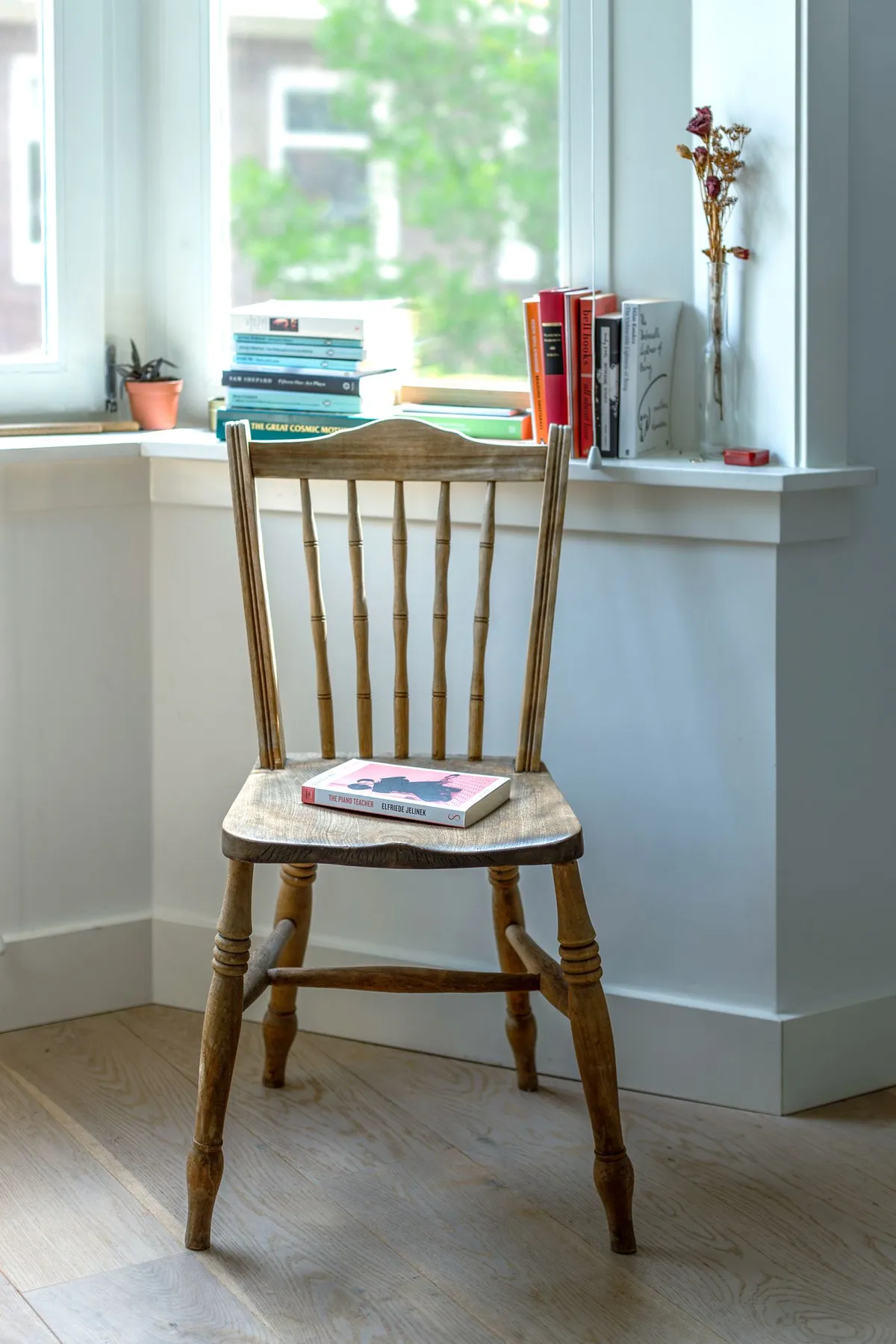 Wooden chair holding books beside a bright window and stacked reading material