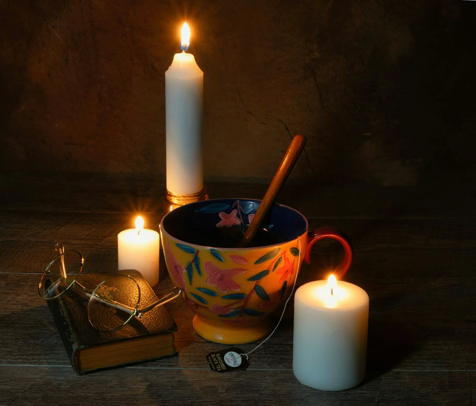 A colourful cup and spoon beside candles, reading glasses and a small book