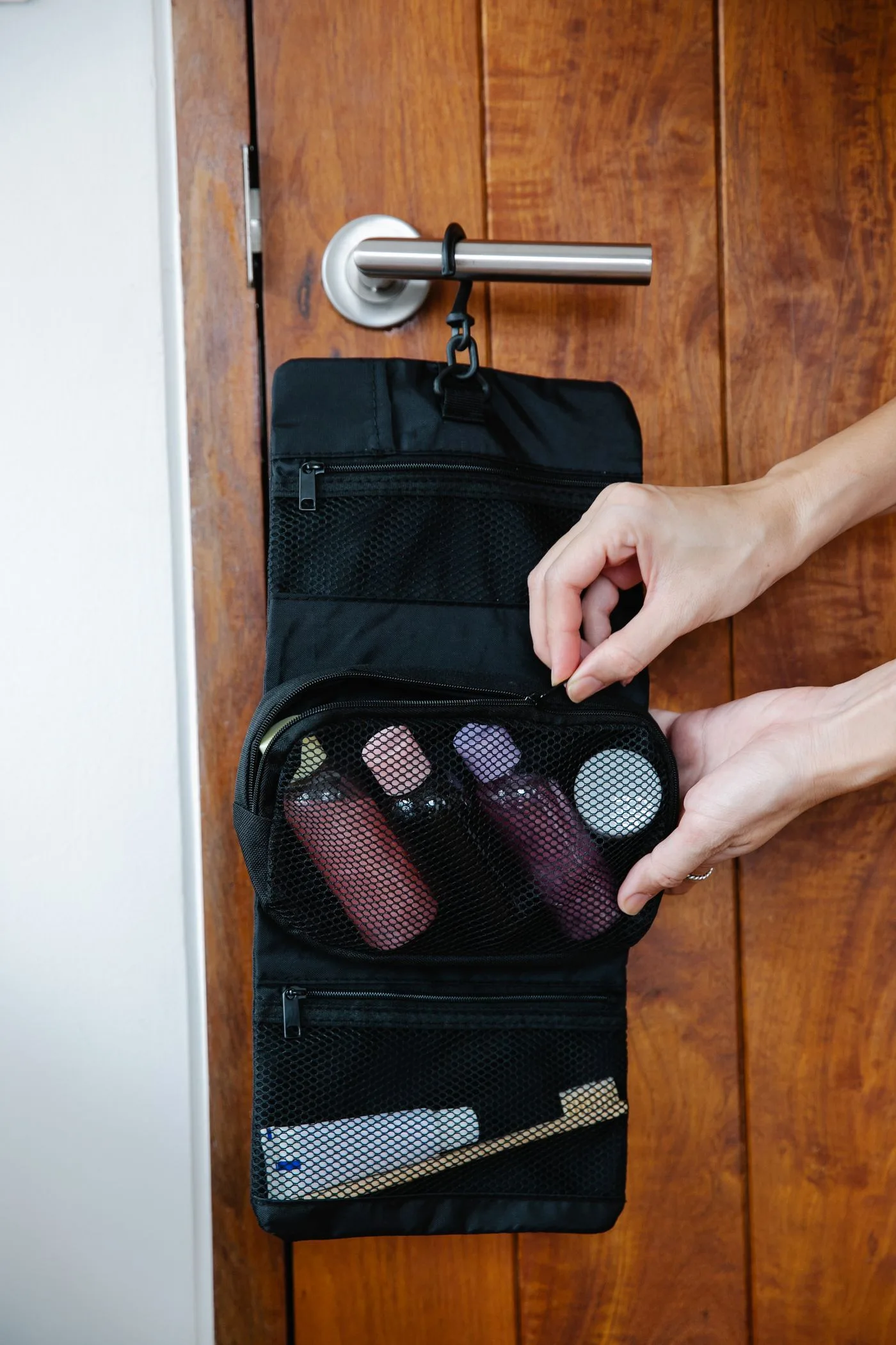 Hands opening a black hanging washbag against a wooden door