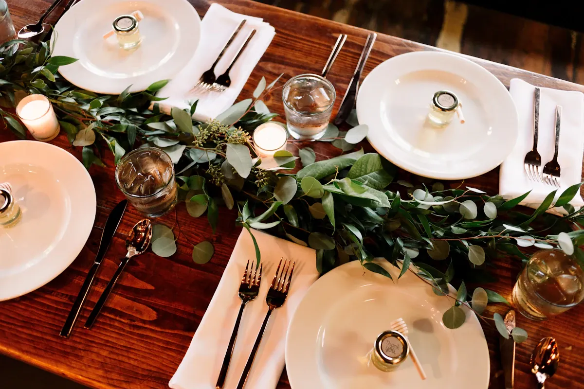 White plates, cutlery and glasses arranged around a leafy dining-table centrepiece
