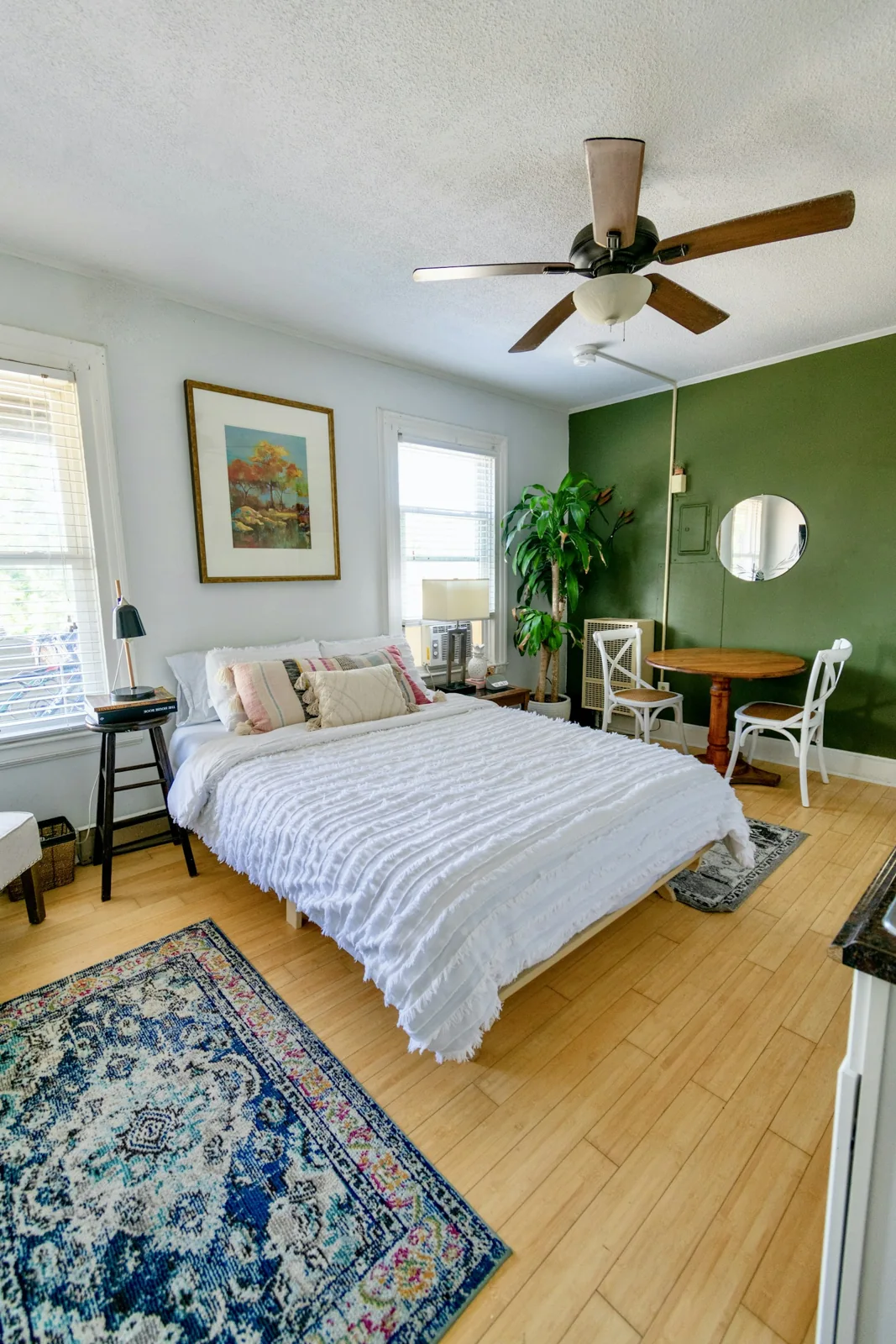 Sunlit bedroom with white bedding, framed pictures and a green accent wall