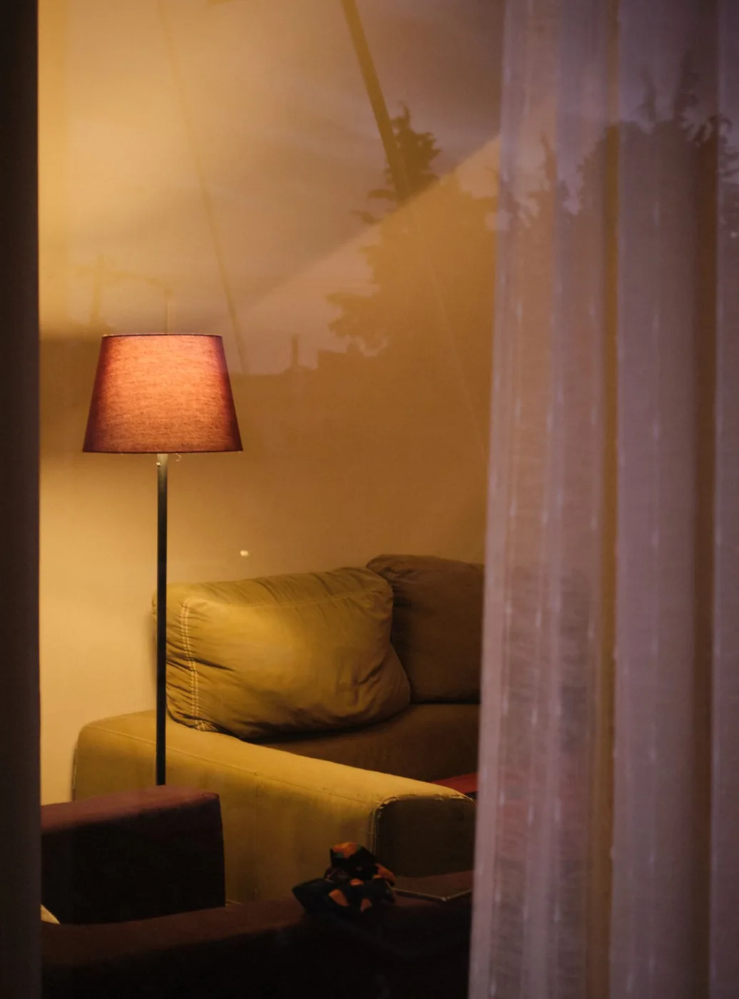 A warm floor lamp beside a sofa and pale curtains