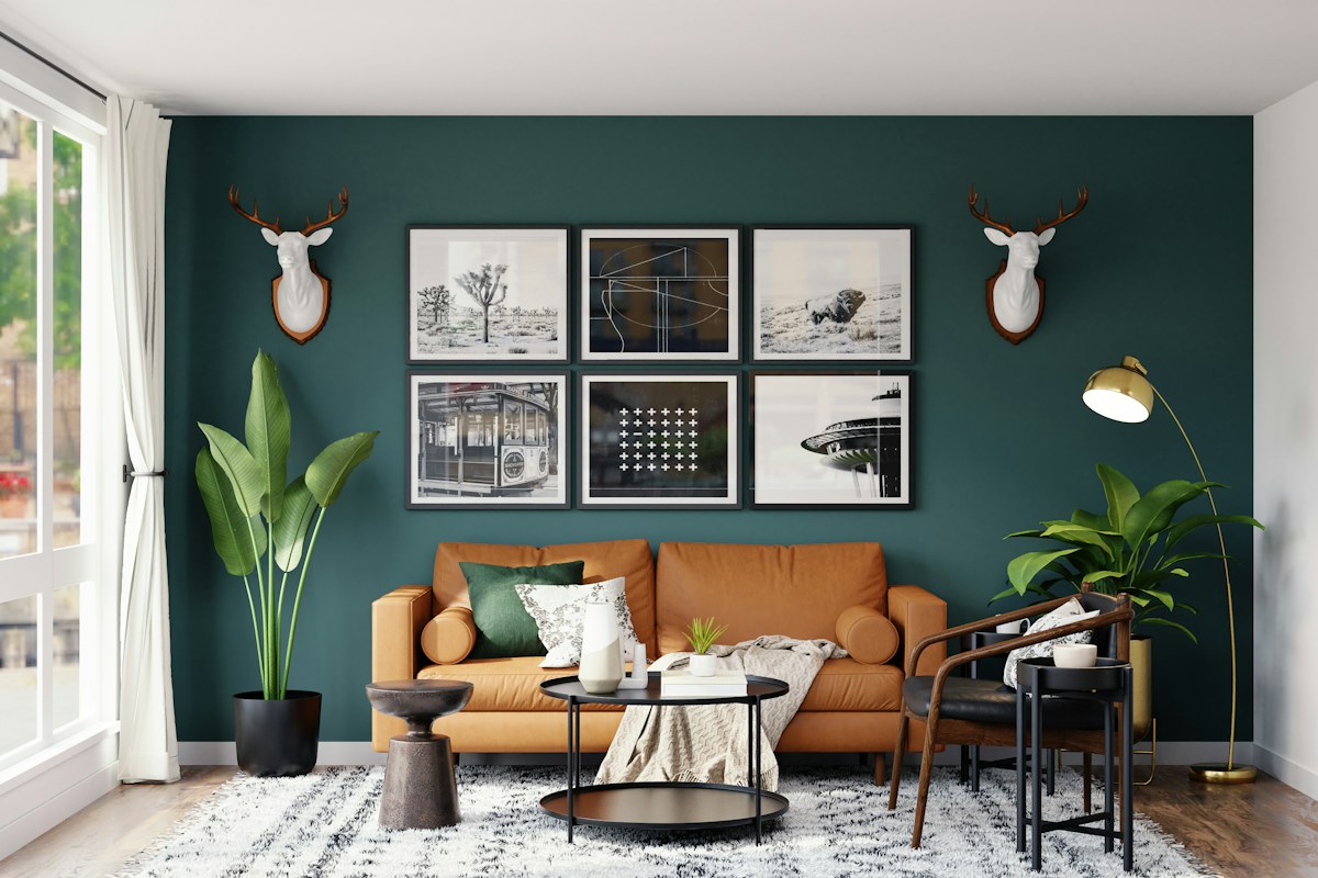A tan sofa with framed pictures against a dark green wall